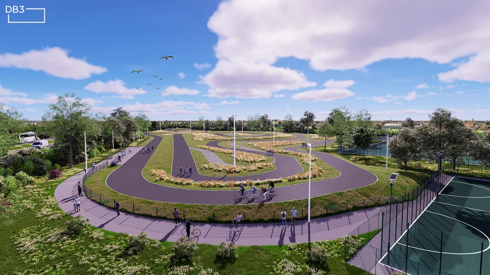 An aerial view of a large cycling pump track with multiple intertwined asphalt paths, surrounded by green grass, trees, and a few people cycling or walking around the track, under a partly cloudy blue sky.